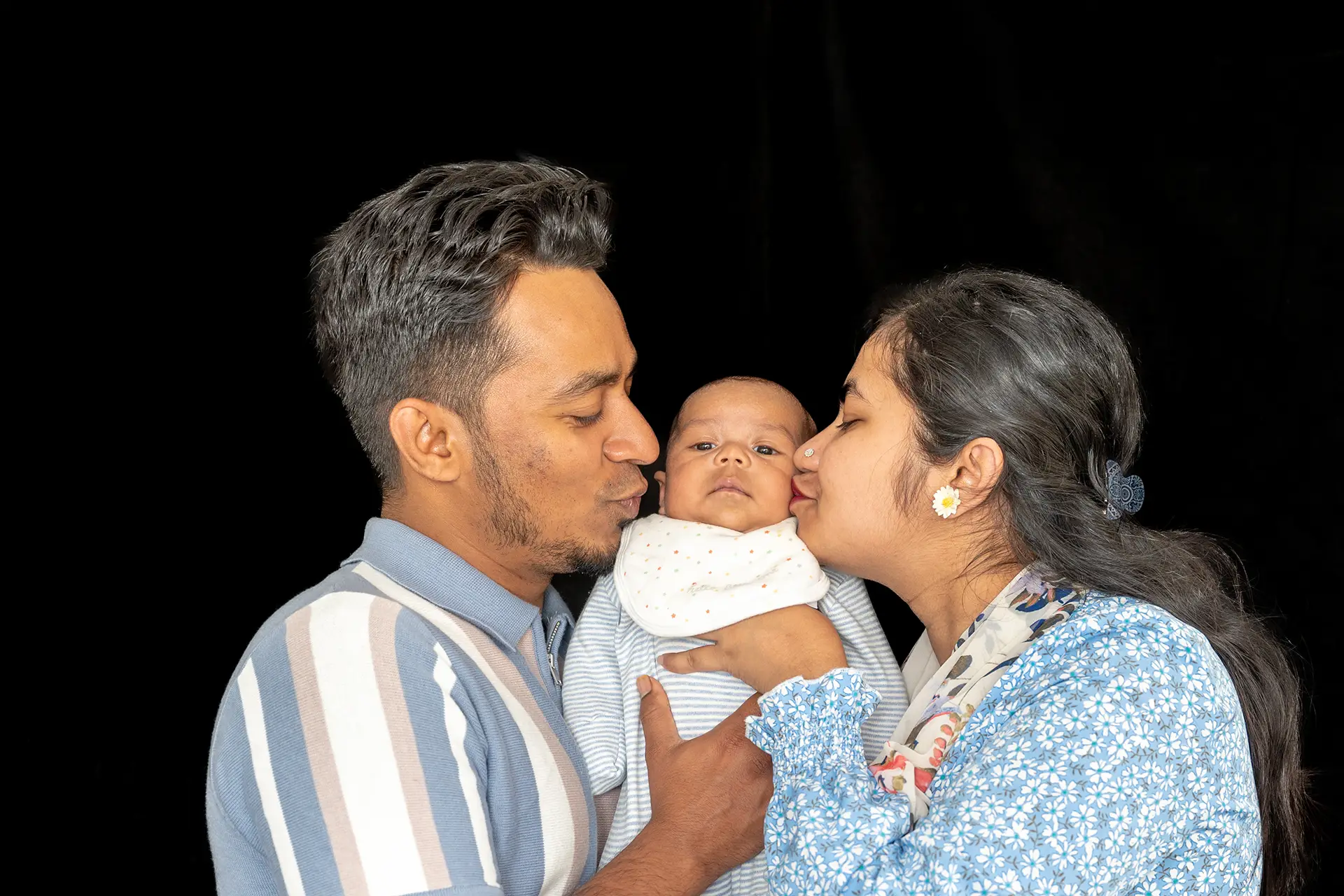 Parents both kissing the cheeks of their baby