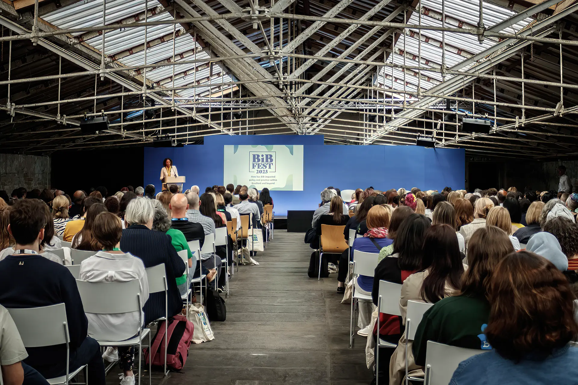 A crowd of people at an event watching a person present on stage.