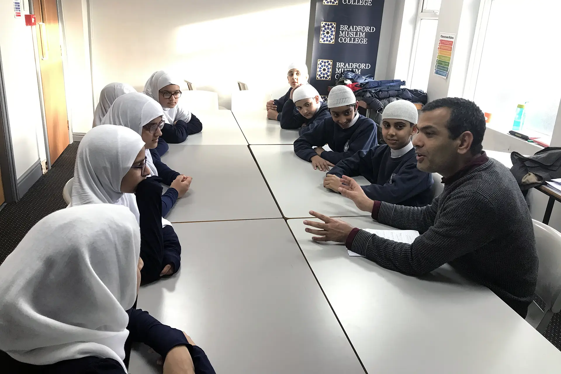 Children sat around a table with teacher at Bradford Muslim College