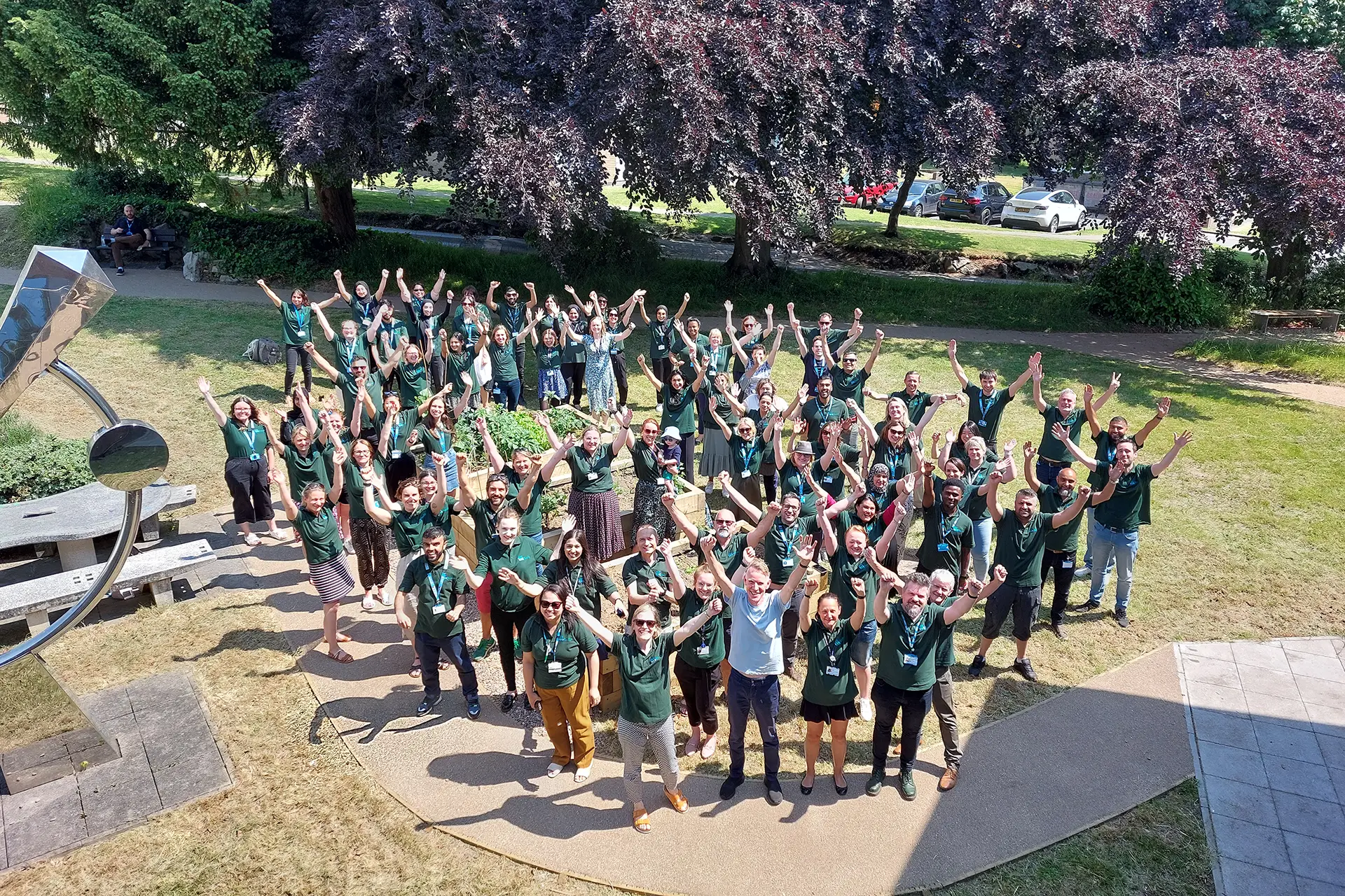 Whole team stood outside celebrating and smiling from the camera. Photo from above.