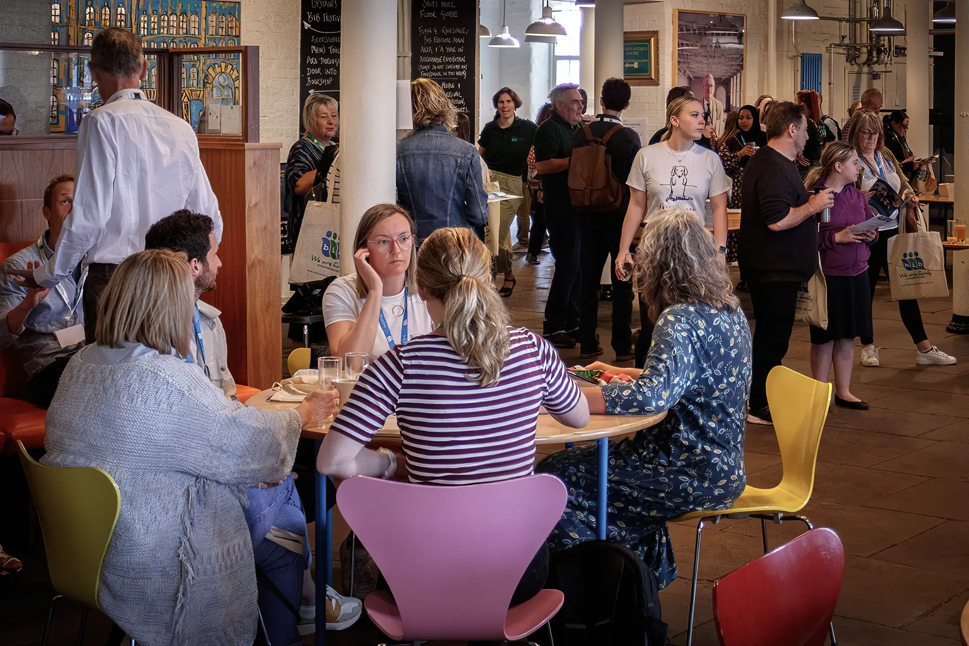 Group of BiB members and general public sat around a table, with further members in background stood around