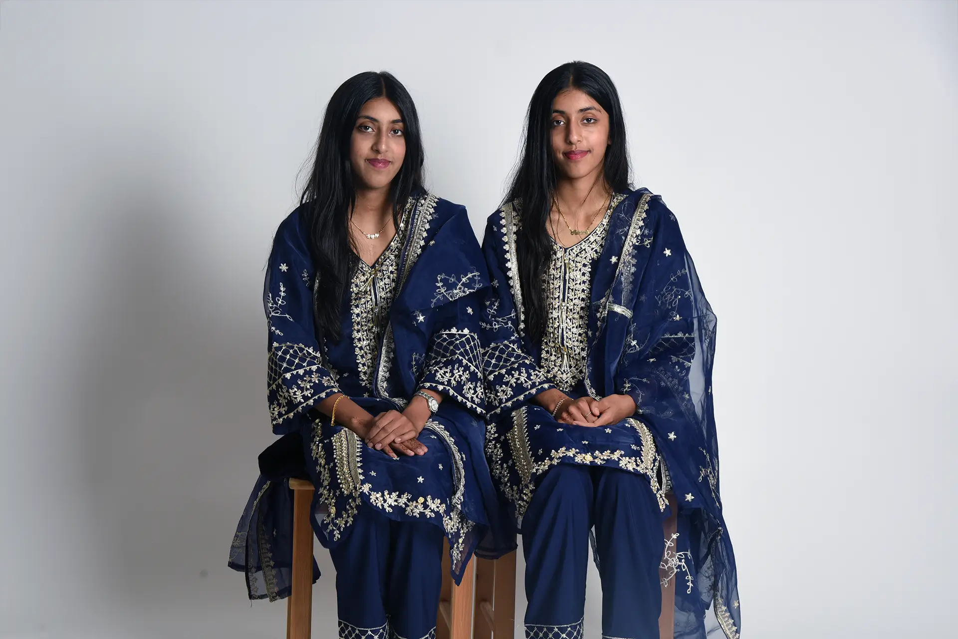 Two twins posing for a photograph, sat on wooden stools. Part of the BiB Twin study.